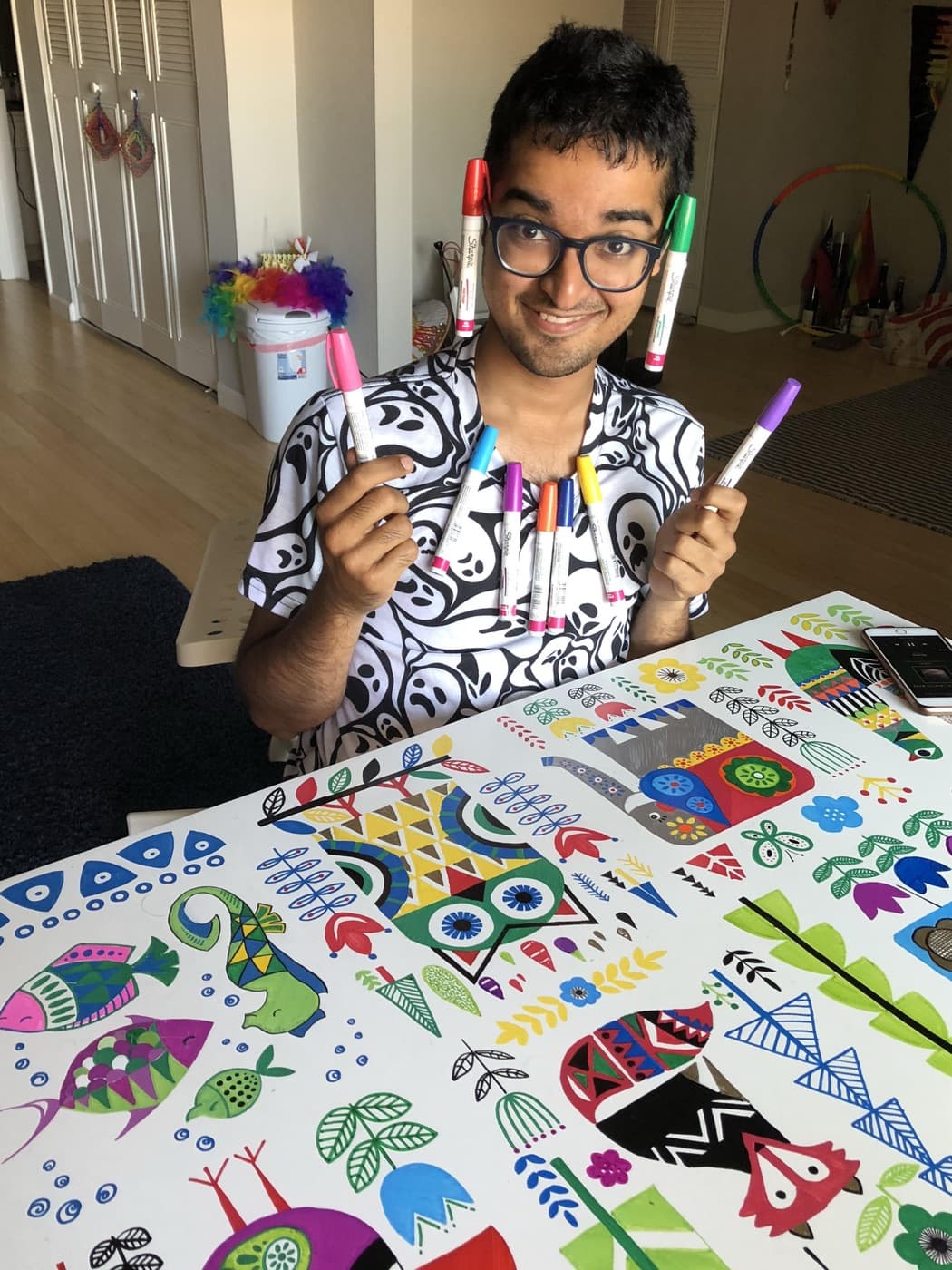 Holding up markers at a table covered in a colorful folk-art painting